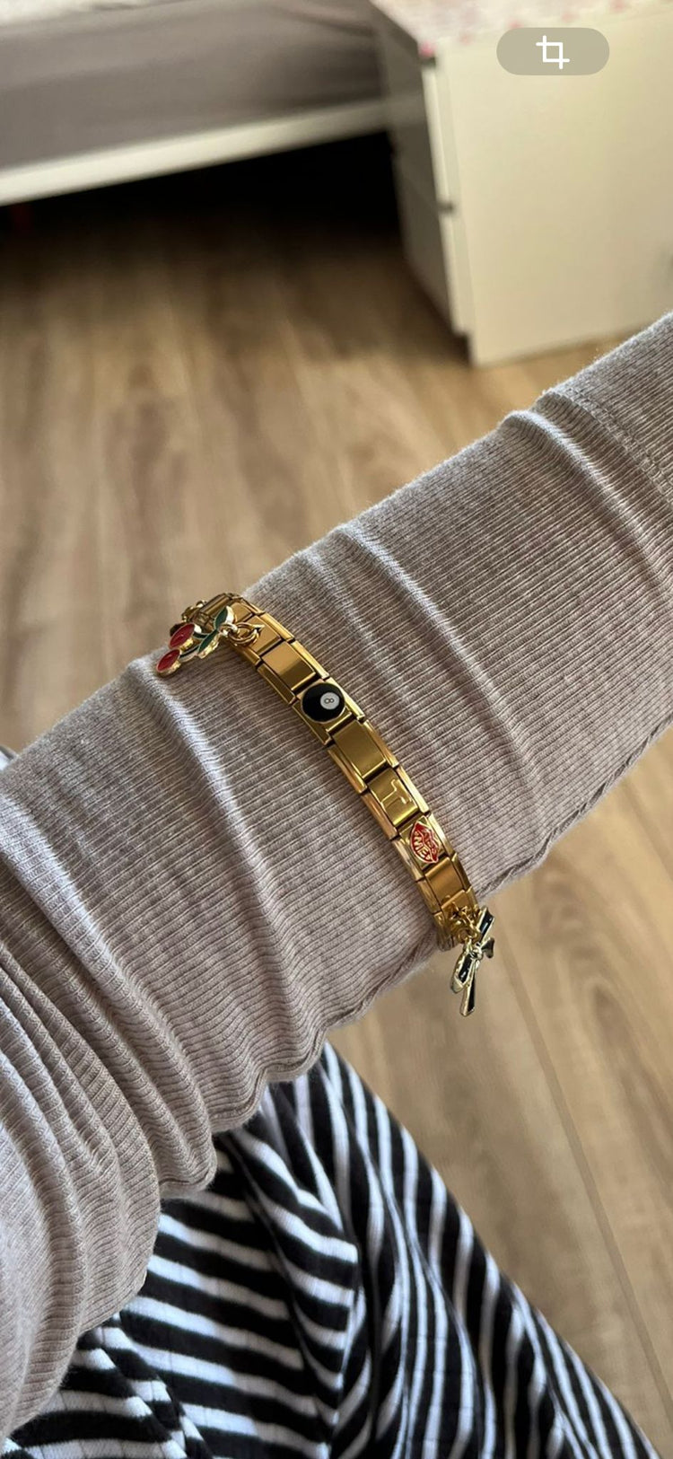 Goldenes Italian Charm Bracelet am Handgelenk, kombiniert mit verschiedenen Anhängern und Charms, getragen über einem beigefarbenen Longsleeve.